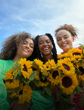 A sharp and vibrant selfie of three people holding flowers.