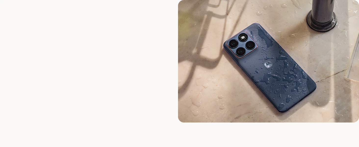 A wet dark blue smartphone with four cameras lies on a cream marble surface beside a metal faucet, droplets of water visible on both phone and surface.