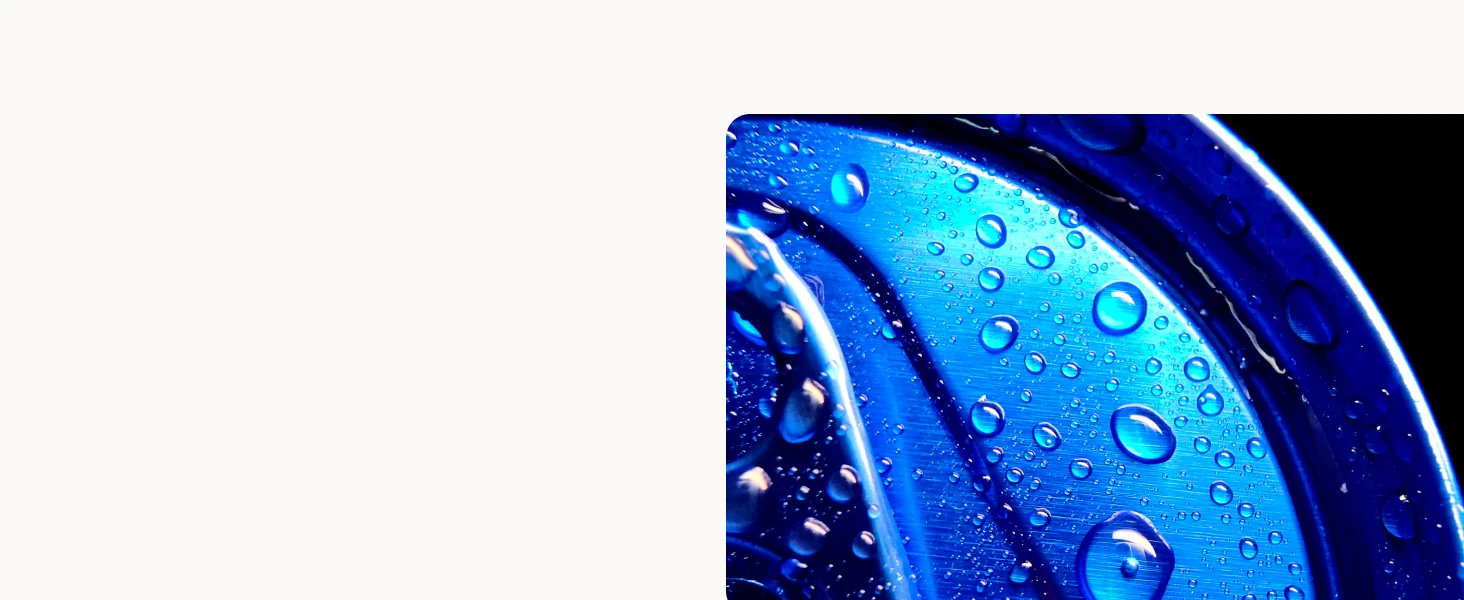 Close-up of the top of a blue aluminium can with water droplets on it, highlighting a shiny surface under light against a black background.