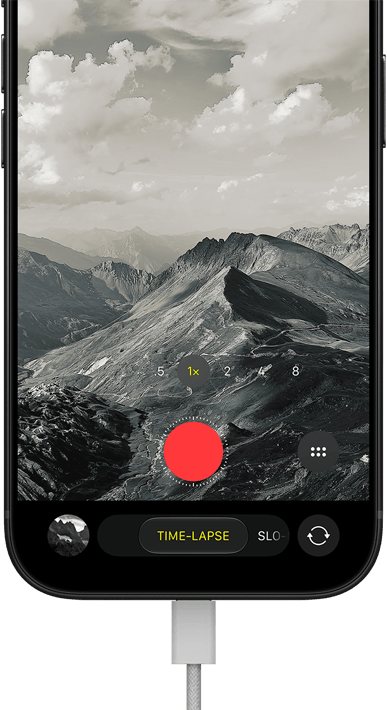 iPhone 18 Pro, front exterior, displaying a mountainous landscape, with the camera mode overlay in Time-Lapse mode, with charging cable attached to charging port