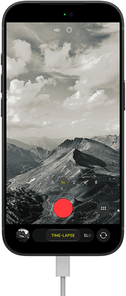 iPhone 18 Pro, front exterior, displaying a mountainous landscape, with the camera mode overlay in Time-Lapse mode, with charging cable attached to charging port
